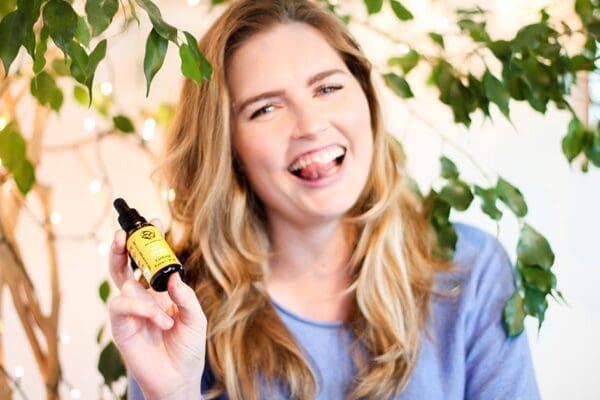 Blond woman laughs, holds Cordyceps supplement bottle, reflecting joy, satisfaction in quality, benefits.